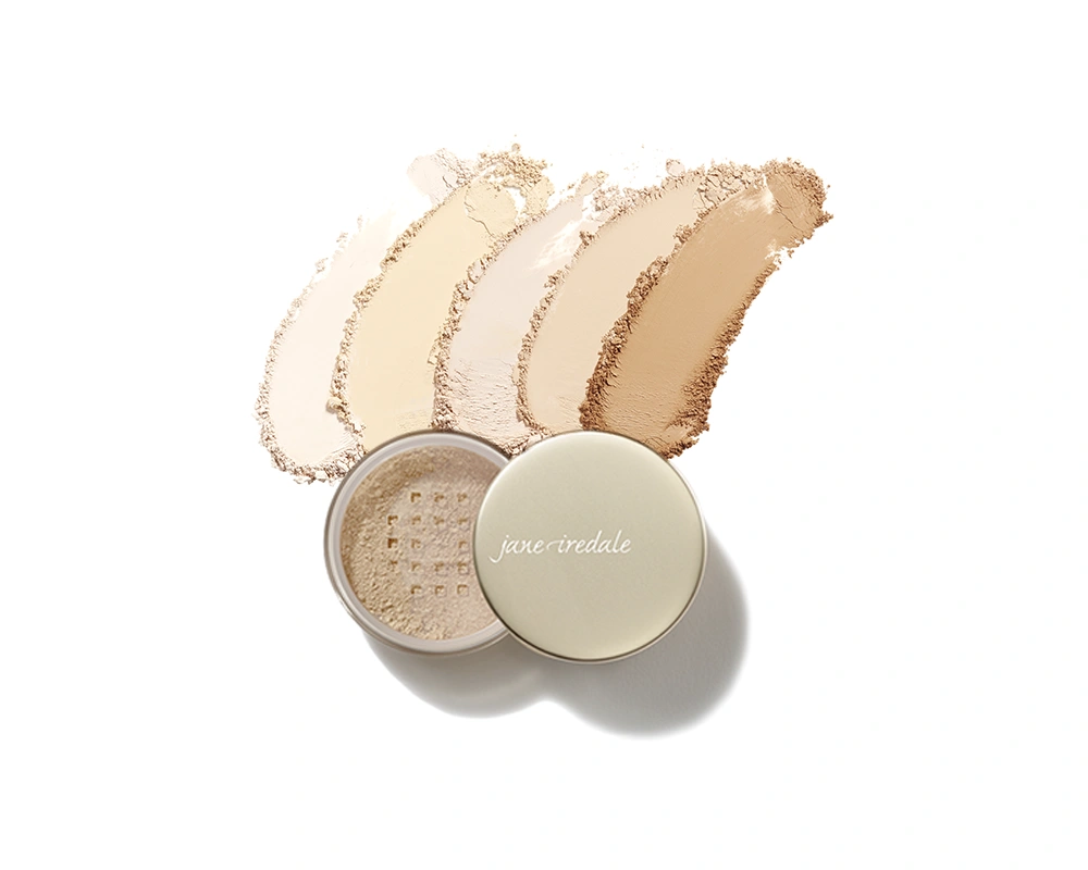 Geöffnete Dose des jane iredale Amazing Base Loose Mineral Powder mit vier aufgetragenen Pudernuancen von hell bis mittel auf weißem Hintergrund
