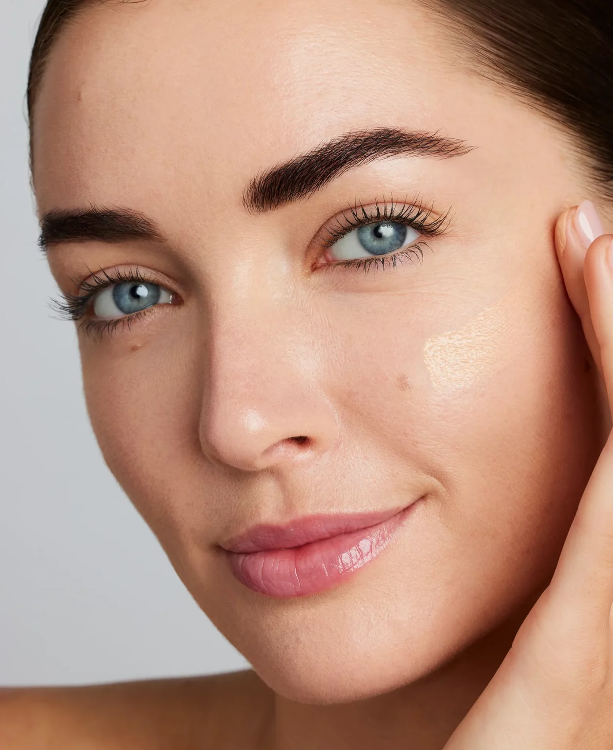 Nahaufnahme eines Gesichts mit dezentem Make-up. Auf der rechten Wange ist ein heller Foundation-Farbton als kleiner Testauftrag sichtbar.