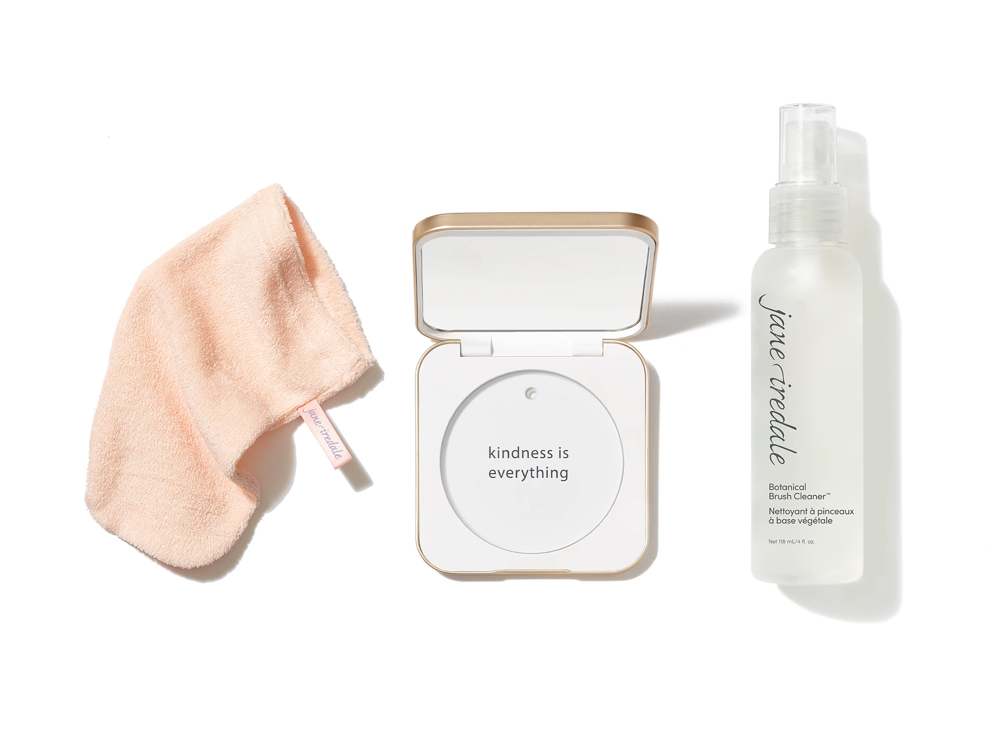Accessoires von jane iredale: pfirsichfarbenes Reinigungstuch, geöffnete Puderdose mit Spiegel und Pinselreiniger in einer Sprühflasche.